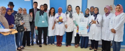 A group of doctors and MS patients pose for a picture. The doctors wear white coats, most of the people in the picture are female and wear headscaves.